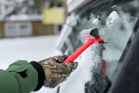 Gloved hand scrape ice from car windshield in winter