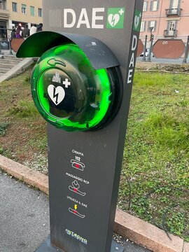 Automated External Defibrillator (AED): A modern AED station is prominently displayed outdoors, its green indicator light suggesting readiness and accessibility for emergency medical use. Pavia, Italy