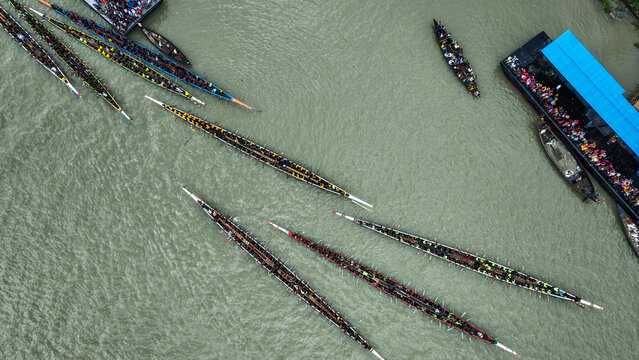 Baghabari, Bangladesh - 20 August 2022: Aerial view of traditional long boats racing on the river with many rowers and spectators on a large boat.