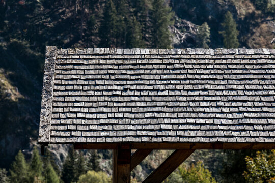 Mountain architecture and rustic construction wooden shingle roof on a traditional alpine cabin with weathered timber texture and natural mountain forest background