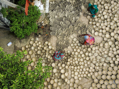 Joypurhat, Rajshahi Division, Bangladesh - 28 September 2026: Aerial view of women in colorful saris working with hundreds of unglazed clay bowls drying on the ground.