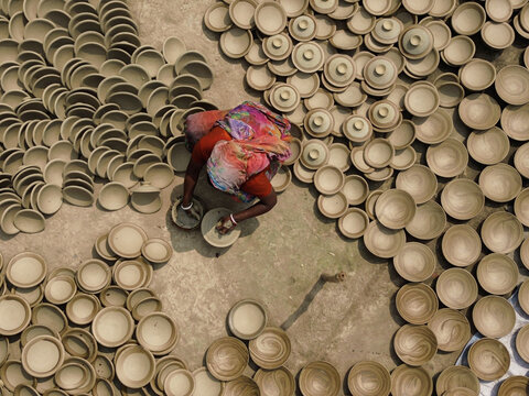 Joypurhat, Bangladesh - 28 September 2026: Aerial view of a woman in a colorful sari crafting clay pottery surrounded by numerous drying bowls and lids on the ground.
