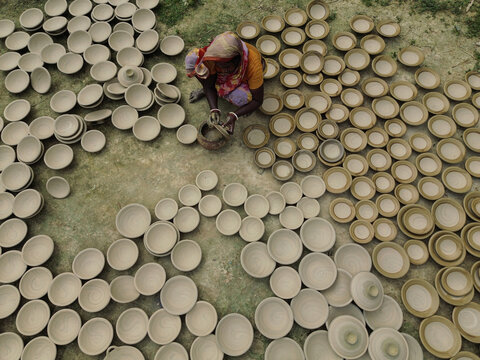 Joypurhat, Rajshahi Division, Bangladesh - 28 September 2026: Aerial view of a potter working with numerous clay bowls laid out to dry on the ground in a rural setting.