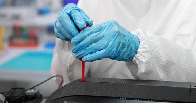 Close-up of a laboratory technician wearing blue gloves and a white coat using a red screwdriver to repair scientific equipment.
