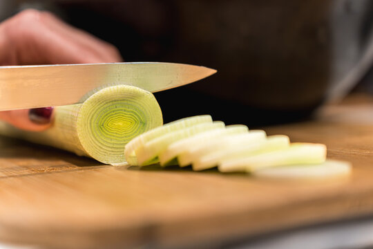 Chef slice leek with knife on wooden cutting board