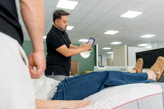 Salesman using smartphone while customer tests showroom mattress