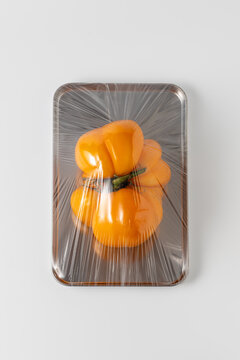 Orange bell pepper wrapped in plastic on metal tray