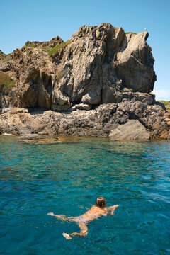 Swimmer in turquoise sea beneath cliffs at Cadaques