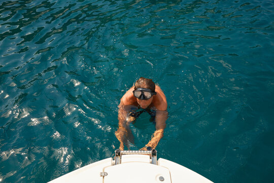 Man with diving goggles climb onto boat from sea