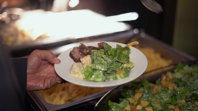 Catering service worker serving salad and meat onto a guest's plate at a luxury buffet event
