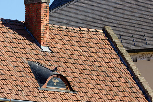 Close-up of an old tiled roof with a brick chimney and a small dormer window