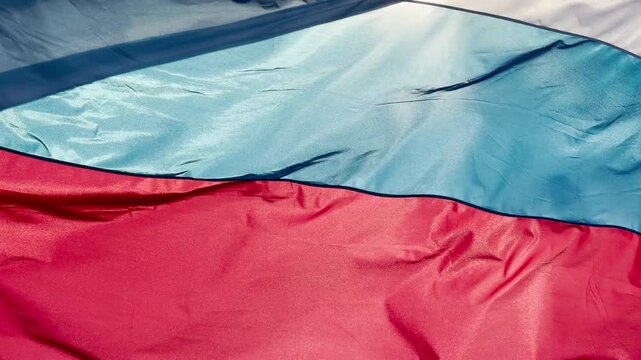 The Russian flag waves proudly, showing its bright white, blue, and red stripes. This flowing fabric creates a patriotic, proud feeling of strength and national unity.