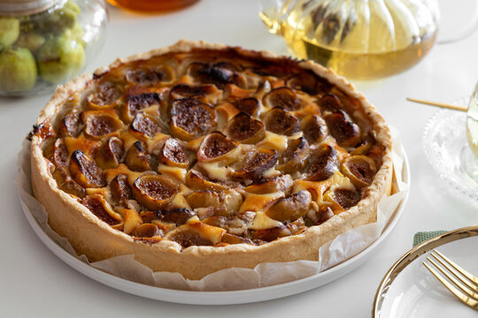Golden brown fig tart freshly baked with flaky crust served on white plate with golden fork
