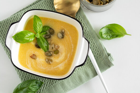 Warm yellow vegetable soup garnished with basil and pumpkin seeds served in white bowl