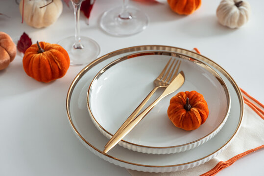 Festive Thanksgiving table setting with small pumpkins and elegant gold cutlery on white plates