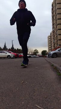 Man jogging toward and past the camera beside parked cars and apartment buildings, ground-level urban running shot, outdoor cardio workout, fitness training, endurance, motivation and active lifestyle