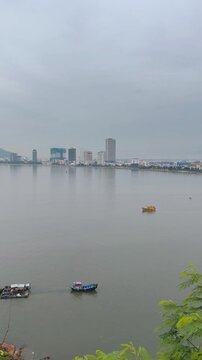 Aerial panoramic view of fishing boats sailing in the foreground with Quy Nhon city skyline in the background, Vietnam. Shot from Hai Minh peninsula featuring calm sea, coastal bay, and cityscape.