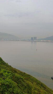 Sweep from Phuoc Mai Lighthouse to Quy Nhon city with fishing boats in foreground, Vietnam. Scenic coastal view from Hai Minh peninsula with lighthouse, sea, mountains, and cityscape.