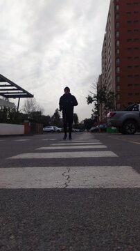 Man running toward the camera across an urban crosswalk, ground-level view of a runner near apartment buildings, outdoor jogging, cardio exercise, fitness training, active lifestyle and determination