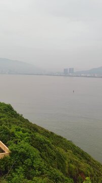 Sweep from Phuoc Mai Lighthouse to Quy Nhon city with fishing boats in foreground, Vietnam. Scenic coastal view from Hai Minh peninsula with lighthouse, sea, mountains, and cityscape.
