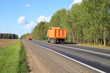 Orange dump trucks on a forest road, back side. Construction equipment driving on the highway. © yaviki