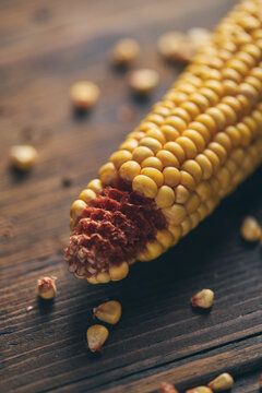 Ripe corn cob with scattered grain on rustic wooden table