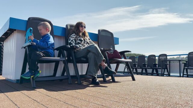 A woman and child relax on deck chairs on a cruise ship at Valaam, Lake Ladoga. This cozy moment evokes a happy, peaceful, and joyful feeling.