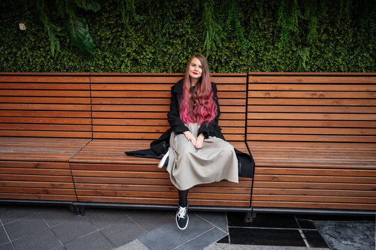 Woman with pink hair sit on wooden bench outdoors