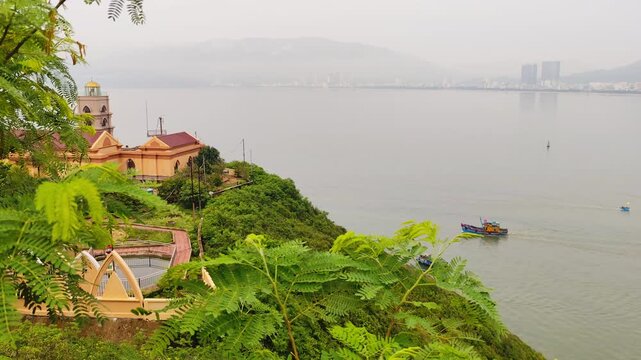 View from Phuoc Mai Lighthouse to Quy Nhon city with fishing boats in foreground, Vietnam. Scenic coastal view from Hai Minh peninsula with lighthouse, sea, mountains, and cityscape.