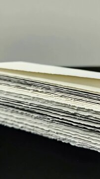 Vertical video: Moving camera revealing deckled paper stack on dark table, showcasing torn edges