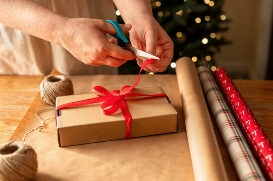Hands tie red ribbon bow on Christmas gift box