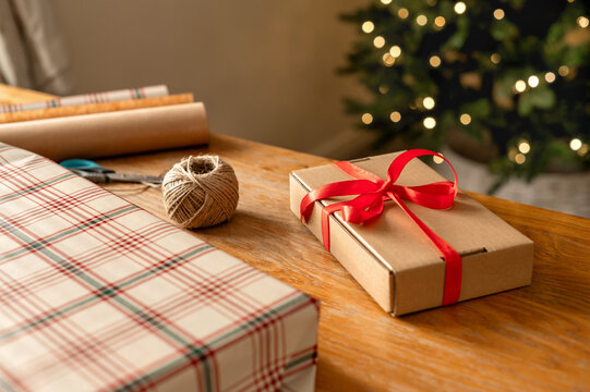 Christmas gift wrapping with ribbon beside decorated tree