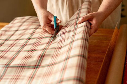 Person cut plaid wrapping paper for gift packaging