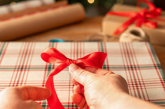 Hands tie red bow on plaid Christmas gift wrapping