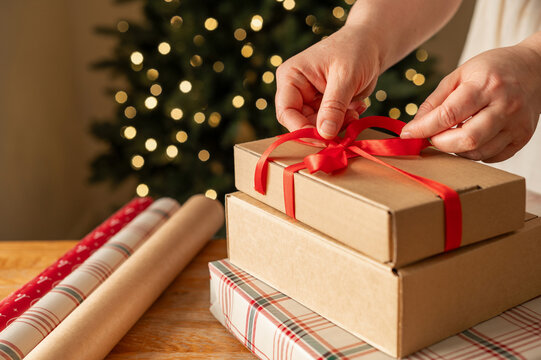 Hands tie ribbon on stacked Christmas gift boxes