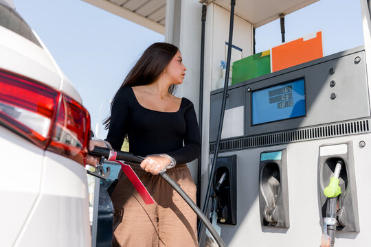 Woman refueling car at gasoline station with fuel pump
