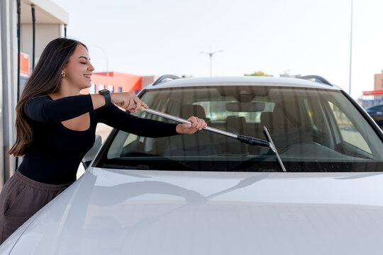 Woman clean car windshield with squeegee at service station