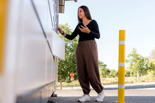 Woman use smartphone at parcel locker for package pickup