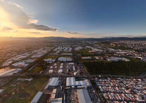 Santiago de Queretaro, Mexico - 18 September 2026: Aerial view of Parque Industrial Benito Juarez with industrial warehouses, storage tanks, and urban landscape at sunset.