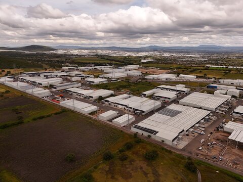 Parque Industrial PyME, Queretaro, Mexico - 18 September 2026: Aerial view of the industrial park with rows of warehouses, paved roads, and surrounding fields under a cloudy sky.