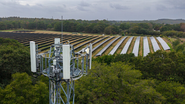 Fleet, England, United Kingdom - 18 September 2026: Aerial view of a mobile phone mast with a large solar farm and rows of solar panels in a rural landscape under a cloudy sky.
