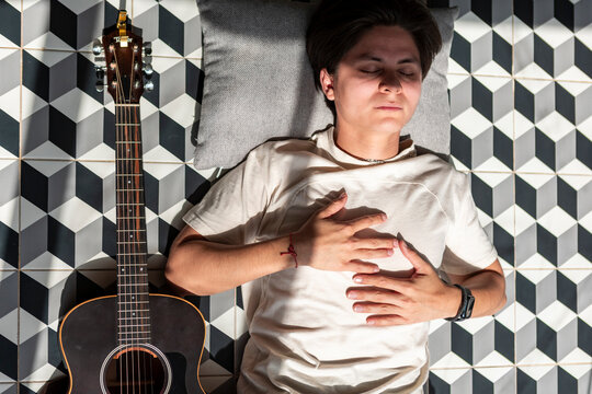 Young musician resting beside acoustic guitar on geometric floor