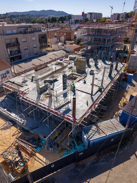 Barcelos, Braga, Portugal - 18 September 2026: Aerial view of a construction site with concrete foundations, steel reinforcement bars, scaffolding, and workers in a developing urban area.