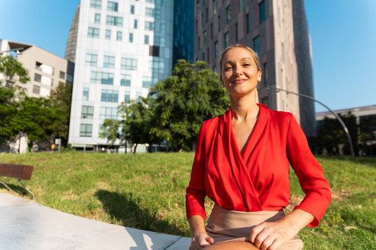 Confident business woman in red blouse in city park