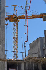 A low angle view of a tall yellow tower crane standing next to an extended white and red concrete pump boom arm at a building construction site © nahhan
