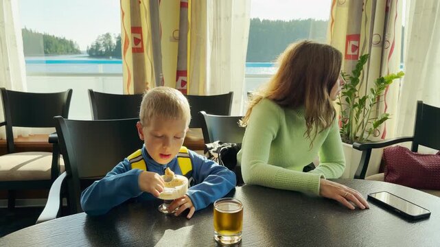 A boy and woman enjoy dessert on a cruise ship at Lake Ladoga. This cozy moment creates a happy, peaceful feeling of warm vacation comfort and serene joy.
