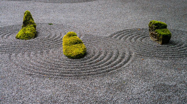 Zen rock garden featuring moss covered stones and raked gravel enclosed by traditional walls at the Portland Japanese Garden in Oregon.