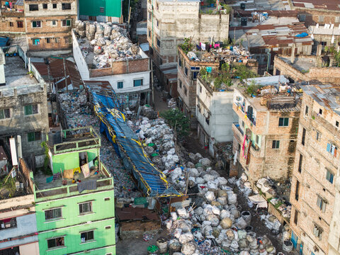 Dhaka, Bangladesh - 27 August 2026: Aerial view of dense urban housing in Dhaka with large piles of collected plastic waste and recyclables stored in bags between residential buildings.