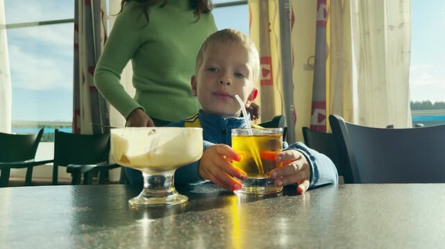 A young boy touches a glass of juice at a table. This cozy scene aboard a cruise ship at Lake Ladoga brings a happy, peaceful feeling of warm vacation joy.