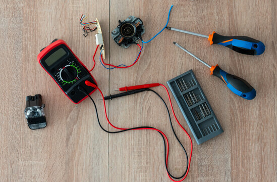 Digital multimeter, probes, screwdrivers, wires and disassembled electronic components arranged on wooden table. Concept of DIY diagnostics, electrical repair, maintenance and technical skills.